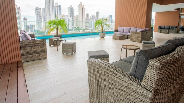 A modern living room with wicker furniture, a city view, and a pool in the background.