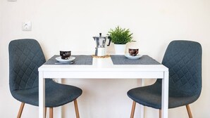 A white table with two dark chairs, a coffee maker, a small potted plant, and two cups of coffee. - Varna Central Studio (Varna)