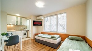 A compact room with a bed, a desk, a washing machine, and a TV displaying the Netflix logo. - Varna Central Studio (Varna)