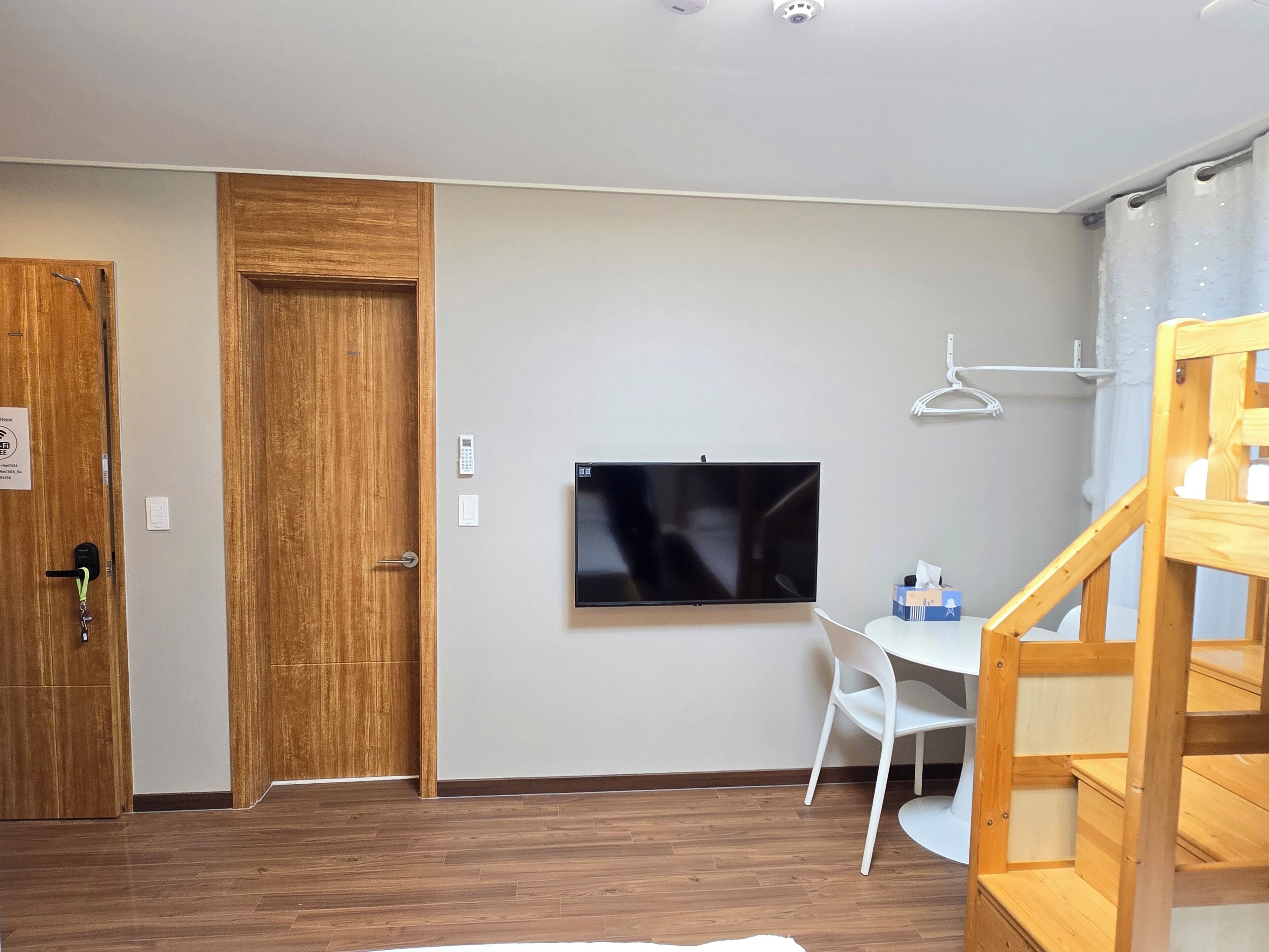 A room with a wooden door, a white desk, a television, and a wooden staircase.