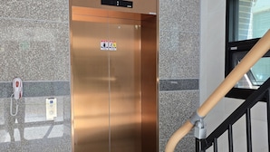 An elevator with a sign indicating accessibility features, a handrail, and a tactile paving strip on the floor. - Incheon Airport Guesthouse L (Incheon)