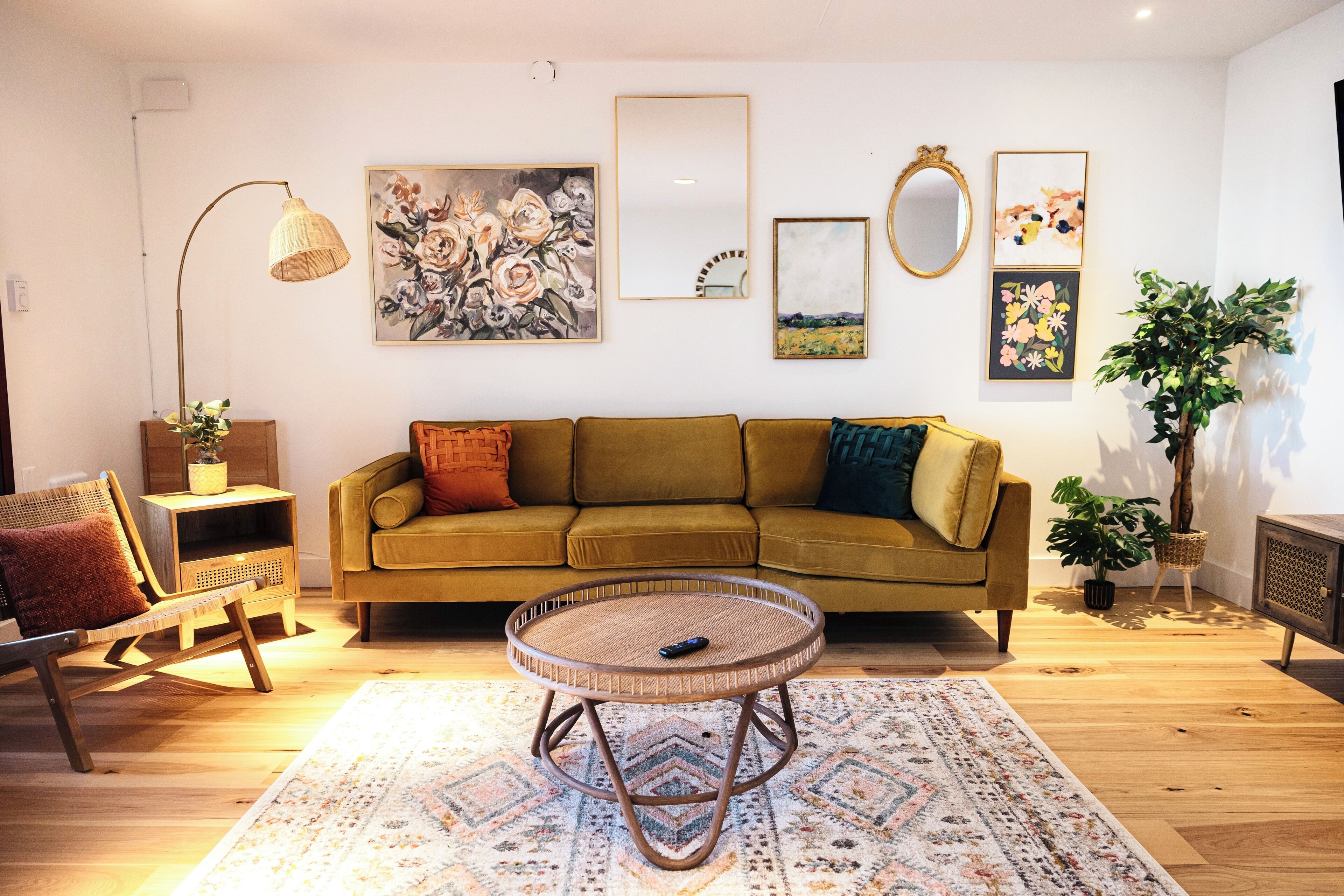 A living room with a green sofa, a round wicker table, and a patterned rug.