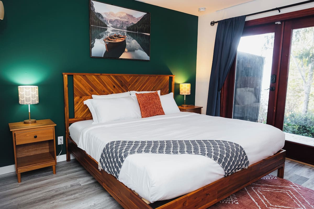 A neatly made bed with white linens and a patterned throw, a wooden headboard, and a nightstand with a lamp.