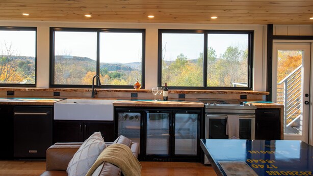 A modern kitchen with large windows, a built-in dishwasher, and a refrigerator. - Amazing 34 foot high shipping container home in Whitingham on Sadawga Lake (Whitingham)