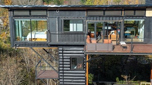 A modern, multi-level cabin with large windows, a balcony, and a staircase. - Amazing 34 foot high shipping container home in Whitingham on Sadawga Lake (Whitingham)