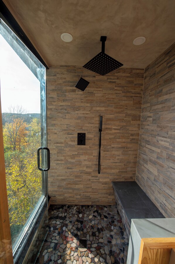 A shower with a stone floor, a window, and a view of trees.