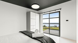 A modern bedroom with a large bed, a wardrobe, and a sliding glass door leading to a balcony with a view of the outdoors. - The Outlook on Mount Louis - 2 Bedroom (Tinderbox)