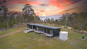 A modern house with a flat roof, large windows, and a deck. - The Outlook on Mount Louis - 2 Bedroom (Tinderbox)