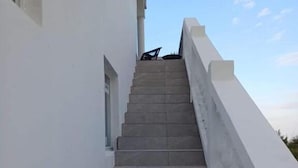Un escalier menant à un bâtiment aux murs blancs, avec un ciel dégagé en arrière-plan.