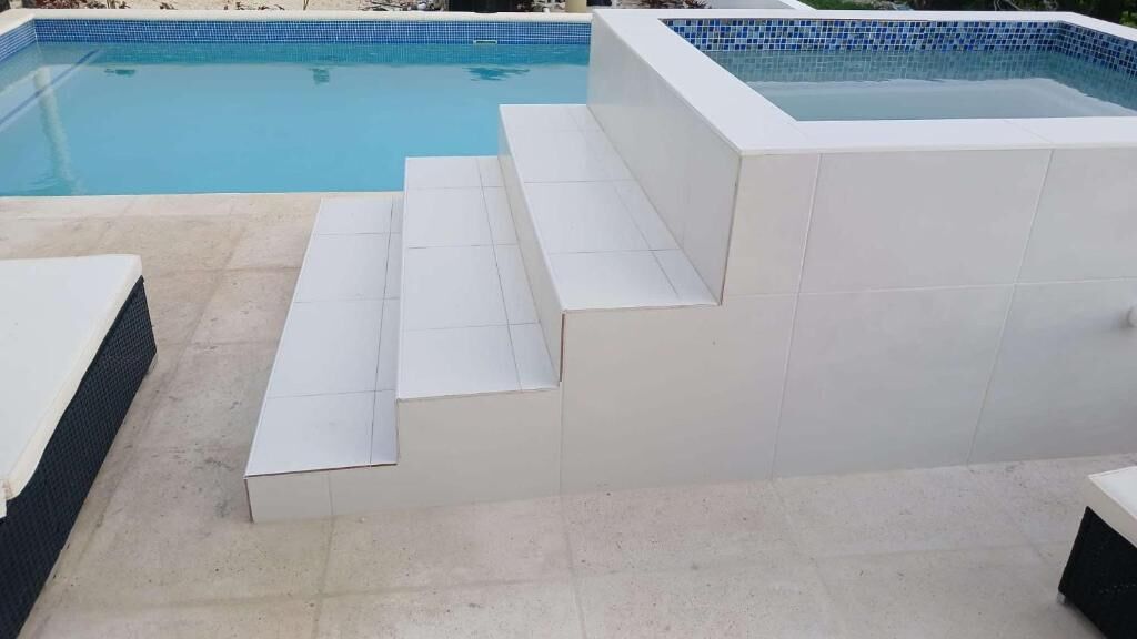 A swimming pool with steps leading into it, surrounded by a tiled deck.