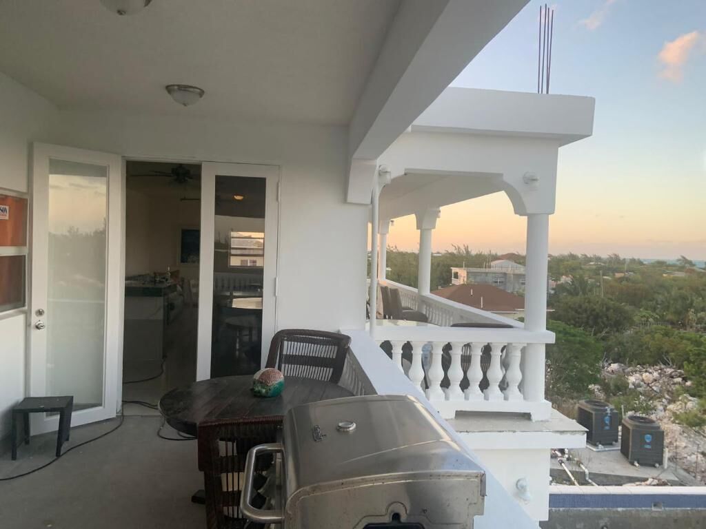 A balcony with a grill, dining table, and chairs, overlooking a residential area.
