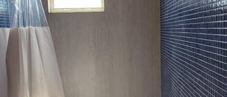 Ein Badezimmer mit Duschvorhang, kleinem Fenster und Fliesenwand.