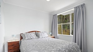 Une chambre à coucher avec un lit, deux tables de chevet, une fenêtre avec des rideaux et une vue sur la verdure à l’extérieur.