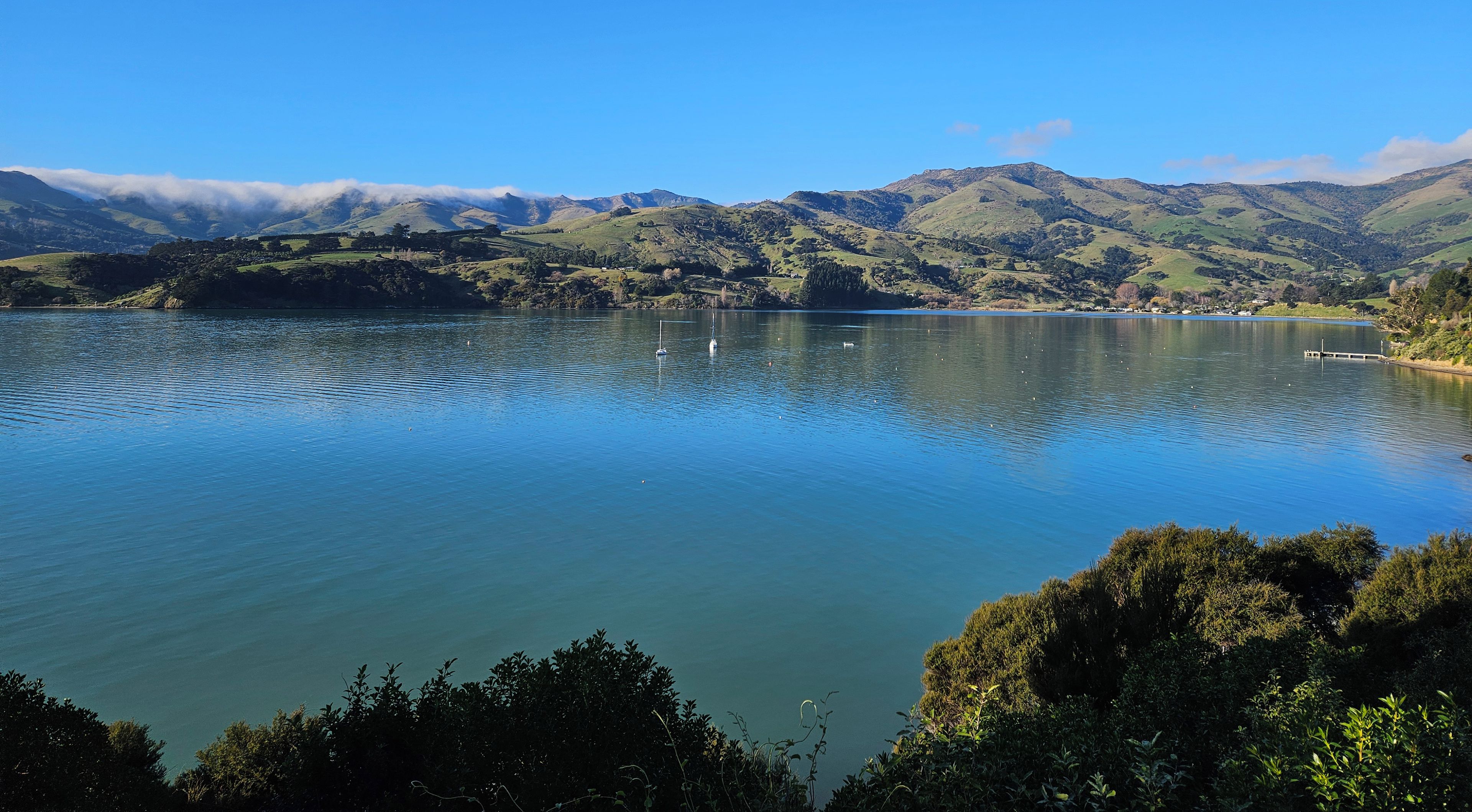 A lake with a dock, surrounded by hills and a clear sky.