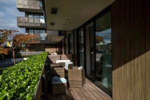 A modern outdoor seating area with wicker furniture and a wooden deck, overlooking a cityscape. - Christchurch Central Apartment, Free Parking, 2-3 Beds (Christchurch)