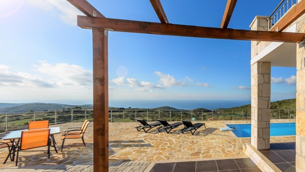 Una terraza con suelo de piedra, una piscina y vistas al mar.
