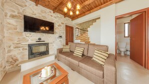 Una sala de estar acogedora con pared de piedra, chimenea, sofá con cojines a rayas y techo de madera.