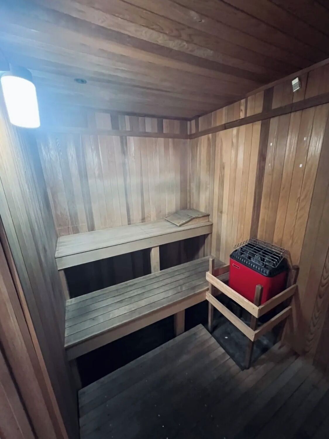 Een houten interieur met een bankje, een kleine tafel en een rode opbergkist.