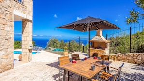 Un espace extérieur aménagé pour les repas, avec un mur en pierre, une table en bois et un barbecue.