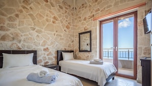 Une chambre d’hôtel avec des murs en pierre, deux lits, un balcon avec vue et un téléviseur fixé au mur.