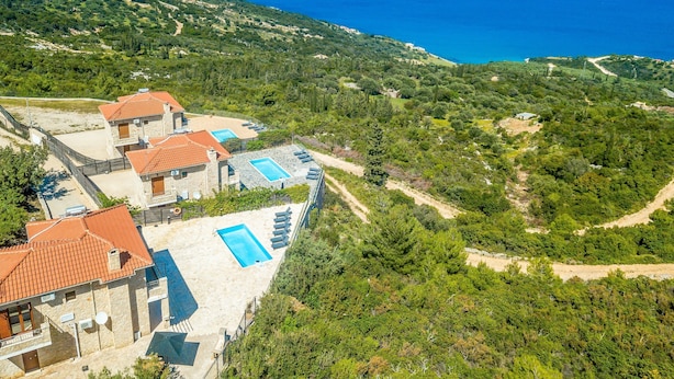 Une propriété située sur une colline, comprenant plusieurs bâtiments, des piscines extérieures et offrant une vue sur la mer.