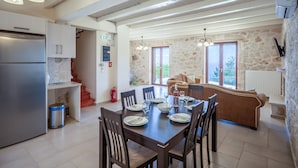 Une cuisine moderne dotée d’un réfrigérateur encastré, un coin repas avec une table dressée pour six personnes, des murs en pierre et une cheminée en pierre.