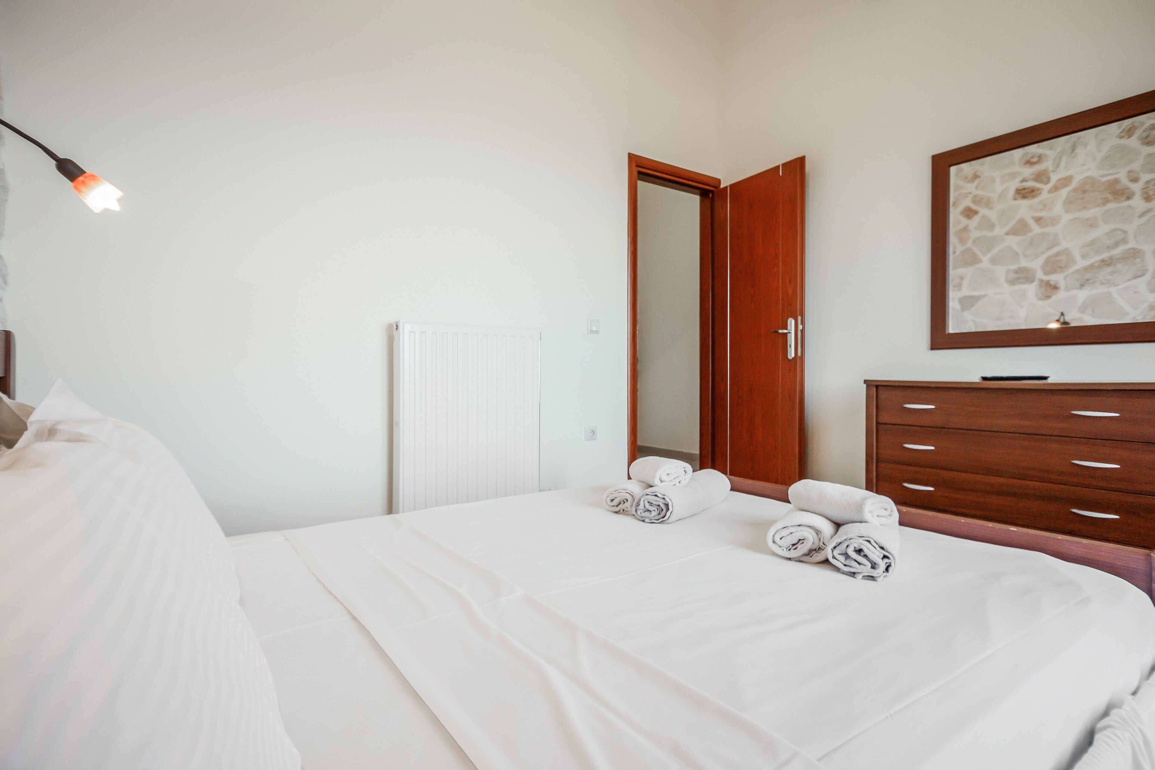Une chambre à coucher avec un lit, une commode en bois, un miroir et une porte.