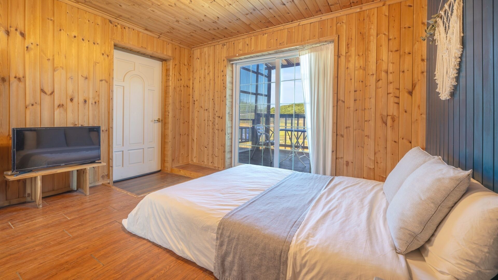Una habitación con paneles de madera, una cama, un televisor y un ventanal corredera que da a una terraza exterior.