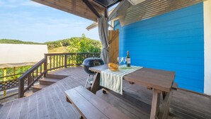 Een houten terras met een tafel voor twee personen, een barbecue en een fles wijn.
