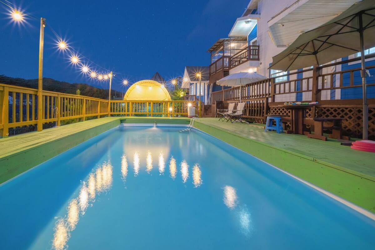 Una piscina con cubierta de madera, cerca amarilla y un edificio con balcón al fondo.