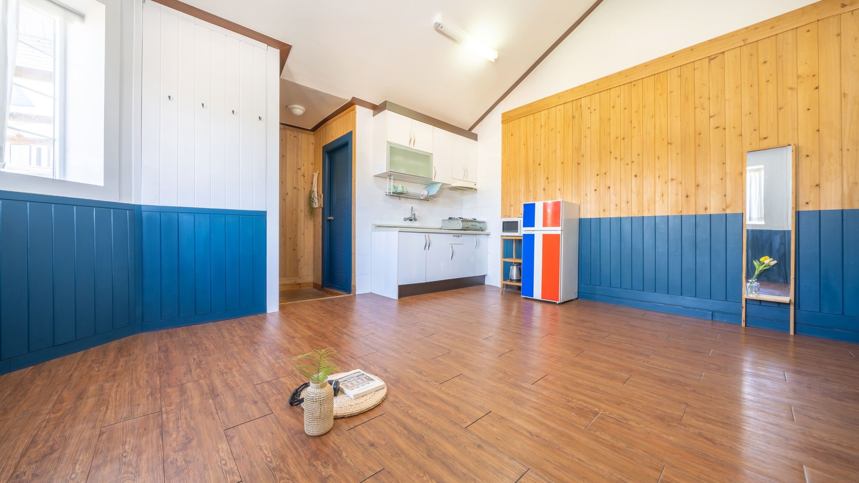Una habitación amplia con piso de madera, una kitchenette y un ventanal grande.