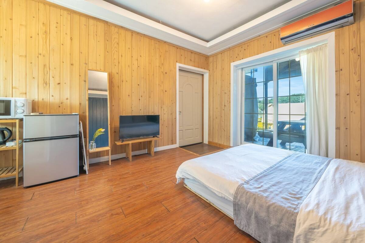 Habitación de hotel con paredes de madera, una cama, un televisor, un refrigerador y una ventana con vistas.