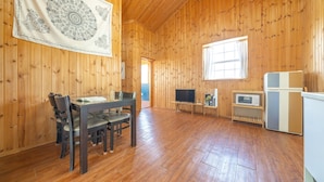 Een kamer met houten lambrisering, een eettafel, stoelen, een televisie, een magnetron en een koelkast.