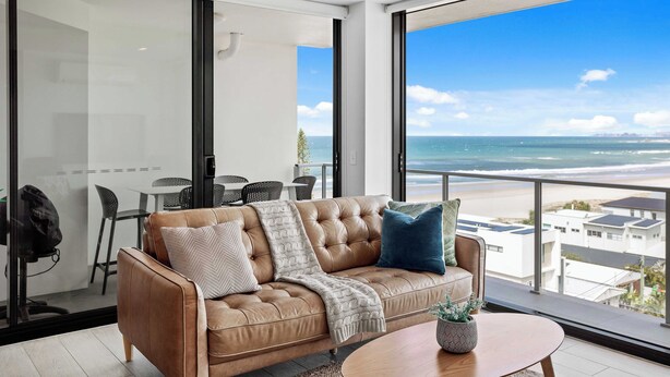 Ein modernes Wohnzimmer mit einer Ledersofa, einem Couchtisch und Blick auf den Strand.