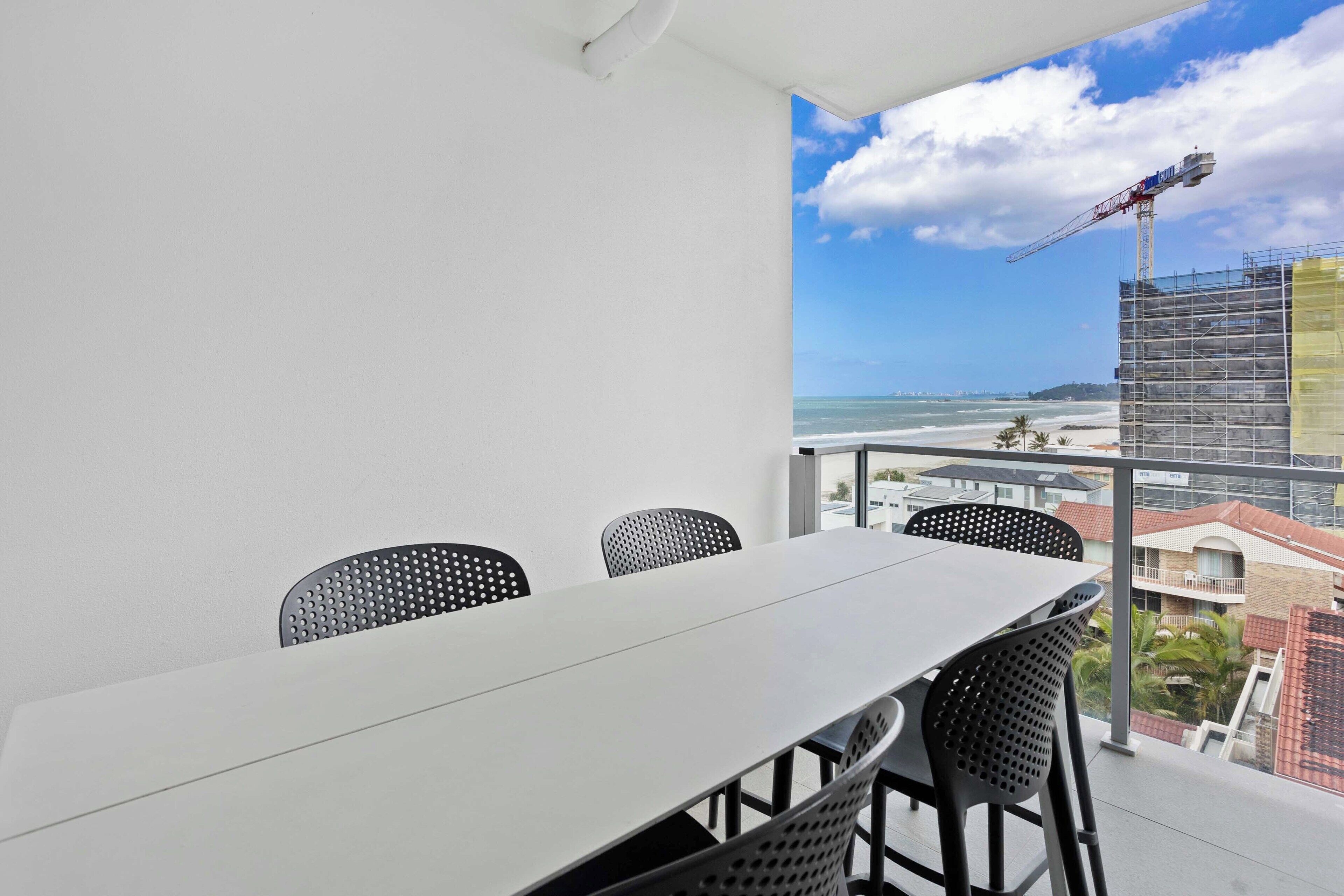 A balcony with a table and chairs, overlooking a beach and a construction crane.