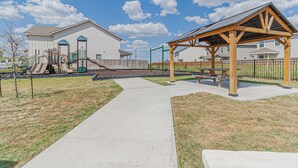 Ein Spielplatz mit Rutschen und Schaukeln, ein überdachter Picknickbereich und ein gepflasterter Weg.