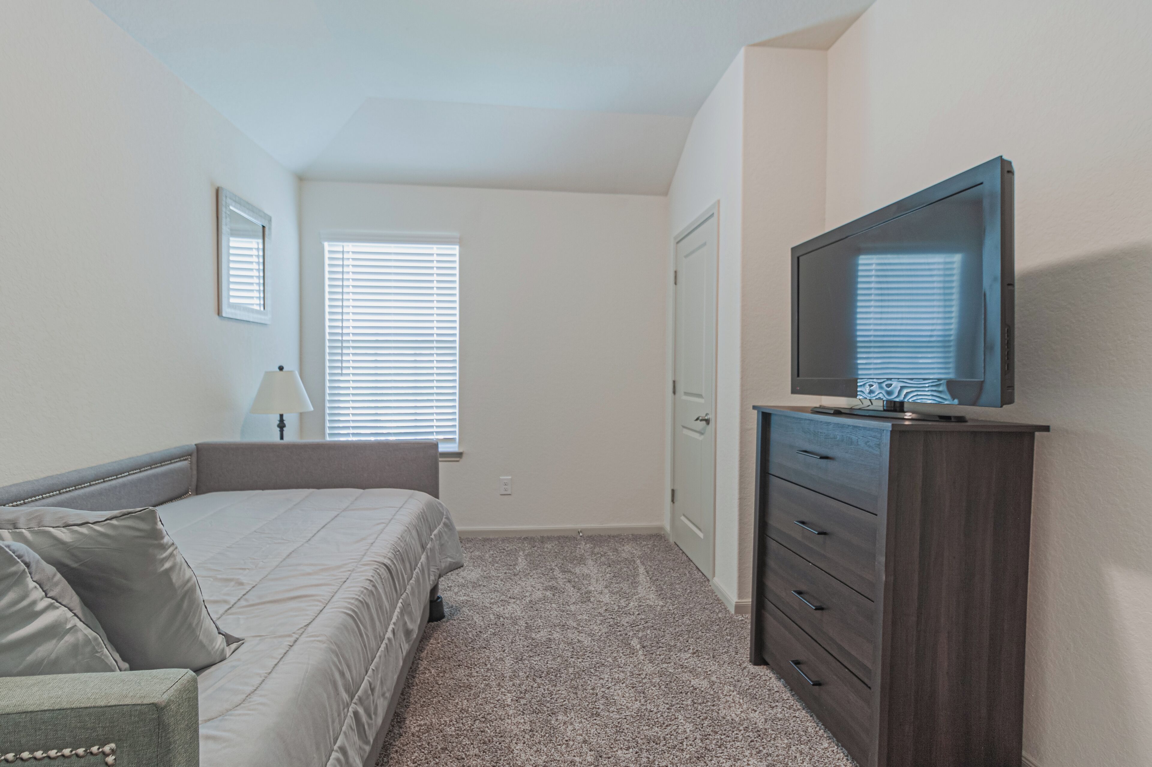 A bedroom with a bed, a dresser, a television, and a window with blinds.
