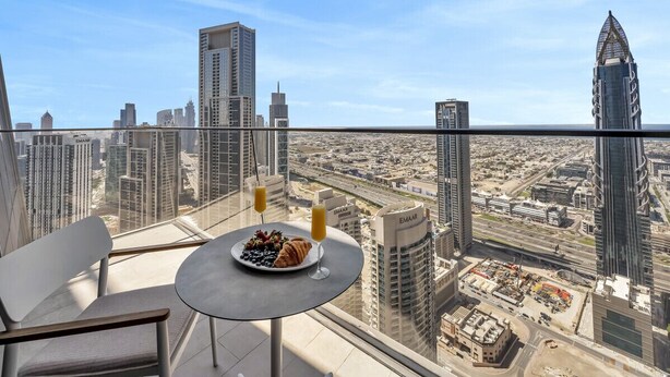 A high-rise balcony with a table set for breakfast, overlooking a cityscape with modern buildings. - Burj Khalifa Pool View Dubai Mall Address Opera 2B (Dubai)