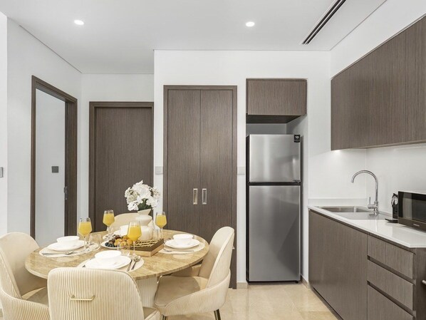 A modern kitchen with a stainless steel refrigerator, a sink, and a dining area with a round table and chairs.