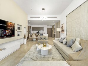 A modern living room with a flat-screen TV, a sofa, a coffee table, and a dining area in the background.