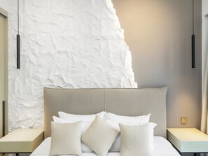 A bedroom with a large bed, two bedside tables, and a textured wall behind the bed.