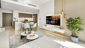 A modern living room with a TV, seating area, and a kitchen in the background. - New 1BR |Burj Khalifa Infinity Pool |Dubai Mall (Dubai)
