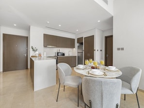 A modern kitchen with a central island, dining area with grey upholstered chairs, and a breakfast setup with orange juice. - New 1BR |Burj Khalifa Infinity Pool |Dubai Mall (Dubai)