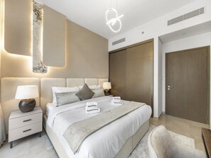 A modern bedroom with a large bed, two bedside tables with lamps, a headboard with built-in lighting, and a wardrobe.