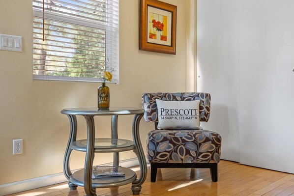 A room with a patterned armchair, a small round table with a vase, and a framed picture on the wall.