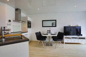Una cocina moderna con horno integrado, un comedor con mesa y sillas, y un televisor de pantalla plana sobre un mueble blanco.