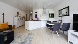 A modern kitchen with white cabinetry, a central island, and a dining area with two chairs.