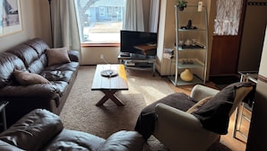A living room with a brown leather sofa, a wooden coffee table, a TV, and a bookshelf. - Large Charcter Home  (Moose Jaw)