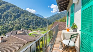A balcony with a view of a mountainous landscape, a table with a chair, and a potted plant. - La Canonica Centovalli with Balconies and Garden, Camedo, Switzerland (Camedo)