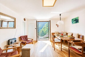 Een modern interieur met een eethoek, een zithoek met een rode stoel, en uitzicht door een glazen deur.